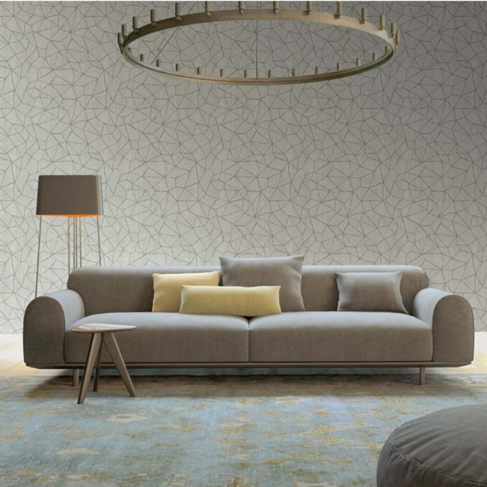 Papel parede creme com formas geométricas, sofá creme com almofadas decorativas, tapete e candeeiro de pé alto