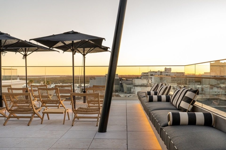 Rooftop com conjunto de mesas e cadeiras de madeira e coxins às riscas branco e azul e almofadas decorativas azuis e amarelas