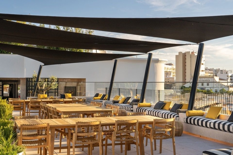 Rooftop with a set of wooden tables and chairs with white and blue striped cushions and blue and yellow decorative cushions