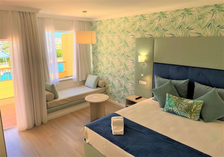 Quarto de hotel com cabeceira de cama verde água e azul, cama com almofadas decorativas azuis e com padrões em tons de verde