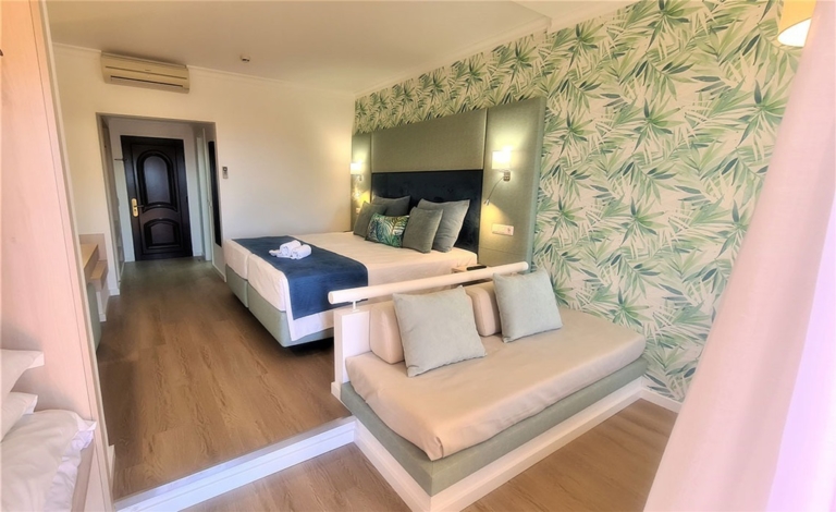 Quarto de hotel com cabeceira de cama verde água e azul, cama com almofadas decorativas azuis e com padrões em tons de verde