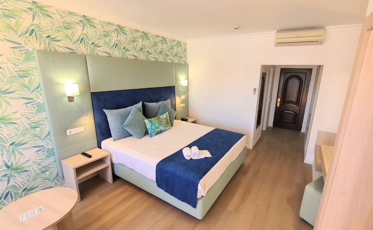 Quarto de hotel com cabeceira de cama verde água e azul, cama com almofadas decorativas azuis e com padrões em tons de verde