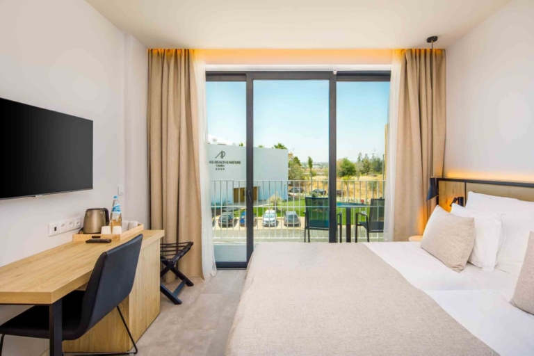 Quarto de hotel com cabeceira de cama, base, colchão tapa pés creme e almofadas decorativas e cortinado em ondas
